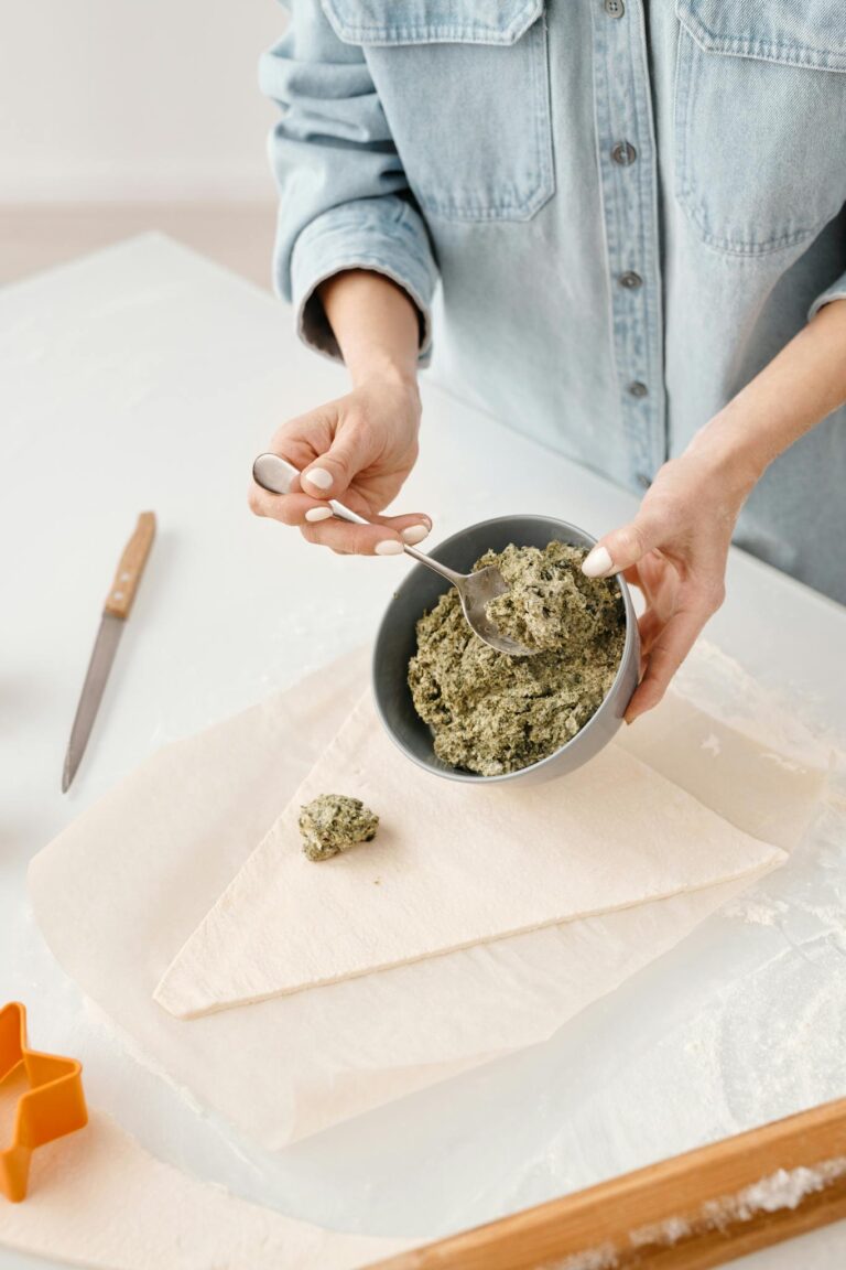 Hands preparing a pastry with fresh green filling, perfect for homemade cooking enthusiasts.