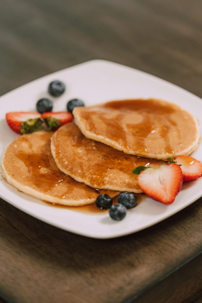 Mouth-watering pancakes served with fresh strawberries, blueberries, and syrup on a white plate.